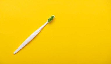 White plastic toothbrush on bright yellow background as flat lay, top view, space for text