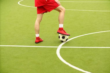 Oyuncular sahada mini futbol oynarlar. Bacaklar, spor ayakkabılar ve bir top. Yeşil futbol sahası.