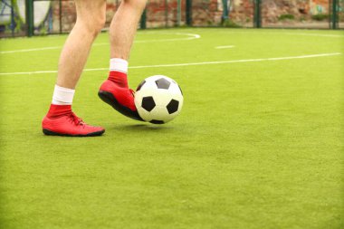 Oyuncular sahada mini futbol oynarlar. Bacaklar, spor ayakkabılar ve bir top. Yeşil futbol sahası.