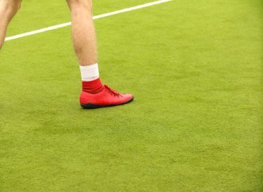 Oyuncular sahada mini futbol oynarlar. Bacaklar, spor ayakkabılar ve bir top. Yeşil futbol sahası.