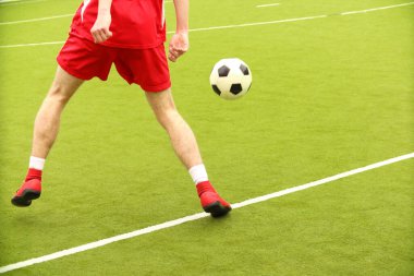 Oyuncular sahada mini futbol oynarlar. Bacaklar, spor ayakkabılar ve bir top. Yeşil futbol sahası.
