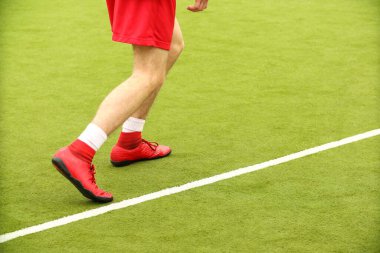 Oyuncular sahada mini futbol oynarlar. Bacaklar, spor ayakkabılar ve bir top. Yeşil futbol sahası.