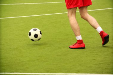 Oyuncular sahada mini futbol oynarlar. Bacaklar, spor ayakkabılar ve bir top. Yeşil futbol sahası.