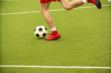 Oyuncular sahada mini futbol oynarlar. Bacaklar, spor ayakkabılar ve bir top. Yeşil futbol sahası.