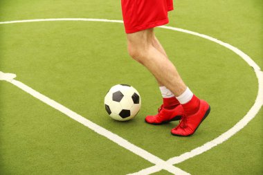 Oyuncular sahada mini futbol oynarlar. Bacaklar, spor ayakkabılar ve bir top. Yeşil futbol sahası.