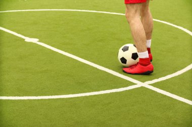 Oyuncular sahada mini futbol oynarlar. Bacaklar, spor ayakkabılar ve bir top. Yeşil futbol sahası.