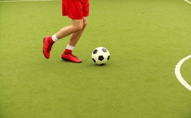 Oyuncular sahada mini futbol oynarlar. Bacaklar, spor ayakkabılar ve bir top. Yeşil futbol sahası.