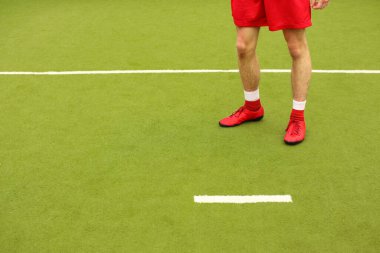 Oyuncular sahada mini futbol oynarlar. Bacaklar, spor ayakkabılar ve bir top. Yeşil futbol sahası.