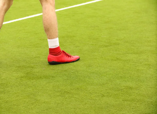 Oyuncular sahada mini futbol oynarlar. Bacaklar, spor ayakkabılar ve bir top. Yeşil futbol sahası.