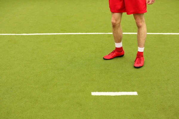 Oyuncular sahada mini futbol oynarlar. Bacaklar, spor ayakkabılar ve bir top. Yeşil futbol sahası.