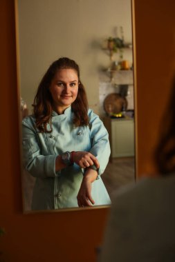 Kadın aşçı işe hazırlanıyor. Önlük giyer, düğmelerini bağlar ve kollarını sıvar.