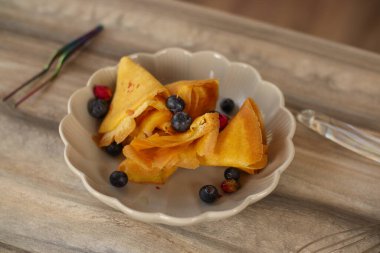 Kadın aşçı, parlak bir mutfakta kırsal tarzda krep hazırlıyor. Nane önlüğü. Böğürtlenli ev yapımı krep. Şef evde.