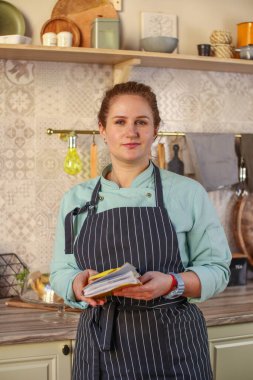 Parlak bir köy mutfağında aşçı kadın. Nane önlüğü ve siyah pantolon giymişti. Yemek hazırlar ve yemek tarifi yazar.