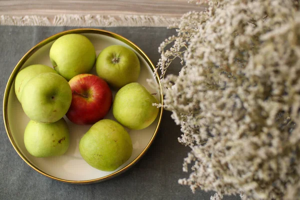 Green and red apples on a white plate with flowers