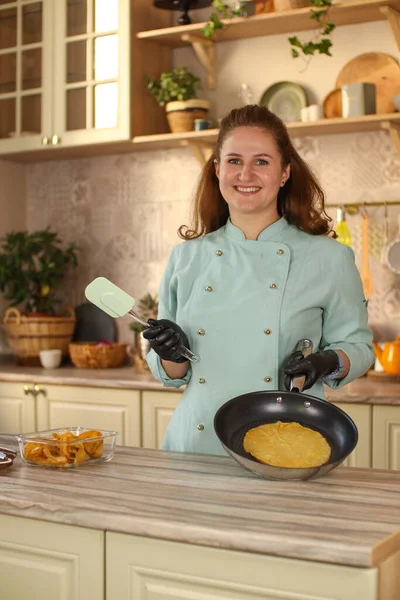 Female chef prepares pancakes in a bright kitchen in a rustic style. Mint coat apron. Homemade pancakes with berries. Chef at home