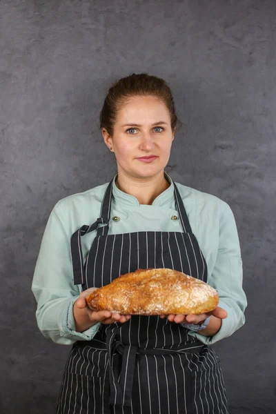 Woman chef on a dark background. Mint coat and black apron. Bread