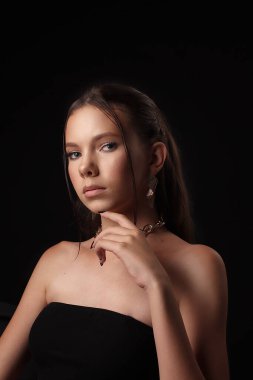 Karanlık bir arka planda genç bir kızın portresi. Güzellik, temiz ten, şık küpeler.