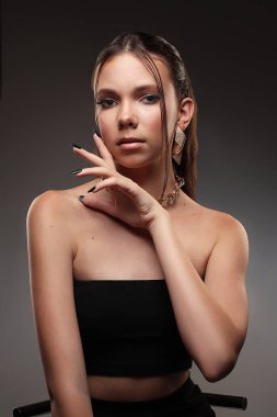 Karanlık bir arka planda genç bir kızın portresi. Güzellik, temiz ten, şık küpeler.