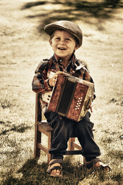 happy young boy playing accordion in summer