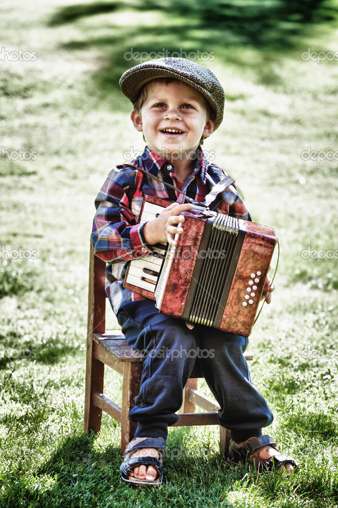 happy young boy playing accordion in summer