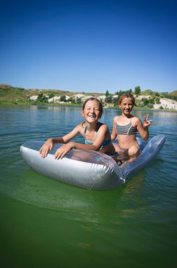 Mayolu iki küçük tatlı kız mavi bir gölde şişme bir yatakta yüzüyor..