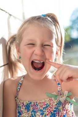 Küçük kız sallanan bir bebek dişini işaret ediyor..