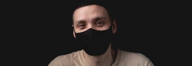 Tecrit edilmiş siyah arka plan üzerinde tıbbi maske takan yakışıklı bir genç. Tek ışık kaynağıyla stüdyo fotoğrafı