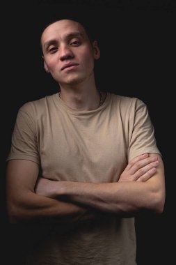 Siyah arka planda poz veren yakışıklı bir genç. Stüdyo fotoğrafı ve tek bir ışık kaynağı. Adam kollarını göğsünde kavuşturmuş duruyor..