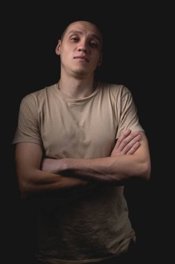 Siyah arka planda poz veren yakışıklı bir genç. Stüdyo fotoğrafı ve tek bir ışık kaynağı. Kafası yukarıda, kolları göğsünün üzerinde duran adam..