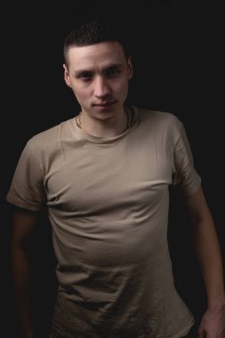 Siyah arka planda poz veren yakışıklı bir genç. Stüdyo fotoğrafı ve tek bir ışık kaynağı. Adam omuzlarını düzeltti ve onun önünde göz korkutucu görünüyordu..