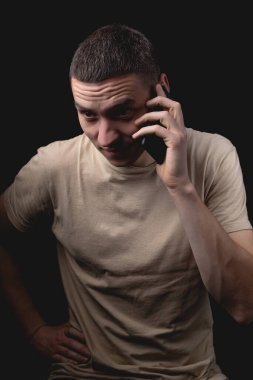 Siyah arka planda akıllı telefonu olan bir adamın stüdyo portresi. Telefonda konuşan yakışıklı bir adam. Tek ışık kaynağıyla fotoğraf.