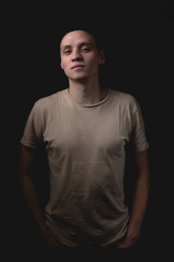 Siyah arka planda poz veren yakışıklı bir genç. Stüdyo fotoğrafı ve tek bir ışık kaynağı. Adam, elleri cebinde onaylayarak önüne bakıyor..