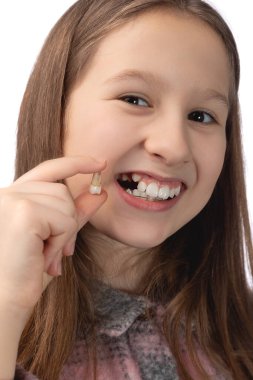 Küçük tatlı bir kız yeni alınmış bir azı dişini elinde tutuyor ve bu dişin çıkarıldığı yeri gösteriyor. Beyaz arkaplanda stüdyo fotoğrafı.