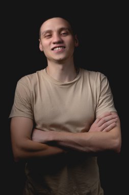 Siyah arka planda poz veren yakışıklı bir genç. Stüdyo fotoğrafı ve tek bir ışık kaynağı. Kolları göğsünde çapraz duran neşeli bir adam..