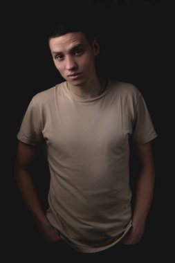 Siyah arka planda poz veren yakışıklı bir genç. Stüdyo fotoğrafı ve tek bir ışık kaynağı. Ciddi bir adam elleri ceplerinde durur..
