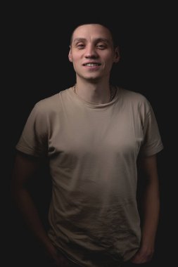 Siyah arka planda poz veren yakışıklı bir genç. Stüdyo fotoğrafı ve tek bir ışık kaynağı. Gülümseyen adam stüdyoda neşeyle poz veriyor..
