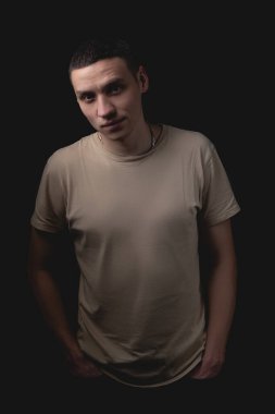 Siyah arka planda poz veren yakışıklı bir genç. Stüdyo fotoğrafı ve tek bir ışık kaynağı. Adam somurtkan bir şekilde önüne bakıyor, öne doğru eğiliyor..
