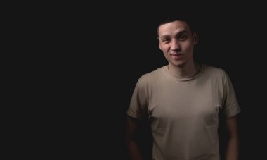 Siyah arka planda poz veren yakışıklı bir genç. Stüdyo fotoğrafı ve tek bir ışık kaynağı. Adam ellerini cebine koyar ve şüphelerini dile getirir..