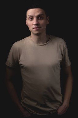 Siyah arka planda poz veren yakışıklı bir genç. Stüdyo fotoğrafı ve tek bir ışık kaynağı. Ciddi bir adam elleri ceplerinde durur..