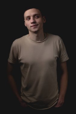 Siyah arka planda poz veren yakışıklı bir genç. Stüdyo fotoğrafı ve tek bir ışık kaynağı. Adam suçunu saklamaya çalışırken kötü niyetli bir şekilde gülümsüyor..