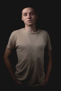 Siyah arka planda poz veren yakışıklı bir genç. Stüdyo fotoğrafı ve tek bir ışık kaynağı. Ciddi bir adam elleri ceplerinde durur..