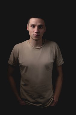 Siyah arka planda poz veren yakışıklı bir genç. Stüdyo fotoğrafı ve tek bir ışık kaynağı. Ciddi bir adam elleri ceplerinde durur..