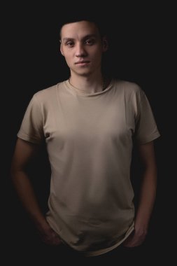Siyah arka planda poz veren yakışıklı bir genç. Stüdyo fotoğrafı ve tek bir ışık kaynağı. Ciddi bir adam elleri ceplerinde durur..