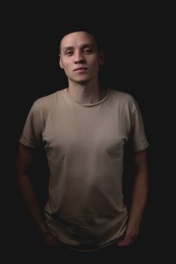 Siyah arka planda poz veren yakışıklı bir genç. Stüdyo fotoğrafı ve tek bir ışık kaynağı. Adam, elleri cebinde onaylayarak önüne bakıyor..