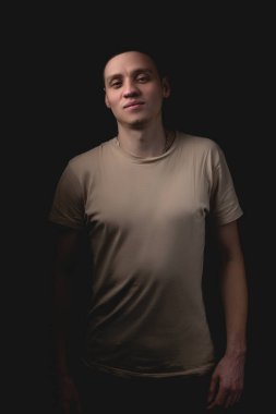 Siyah arka planda poz veren yakışıklı bir genç. Stüdyo fotoğrafı ve tek bir ışık kaynağı. Gülümseyen adam stüdyoda neşeyle poz veriyor..