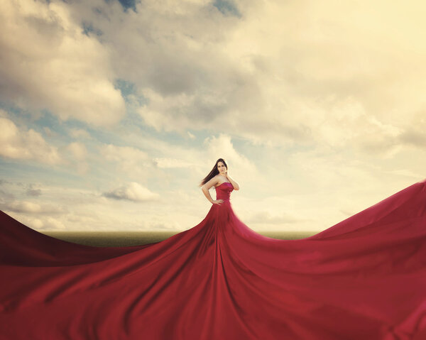 A woman standing in a field with a huge red dress.