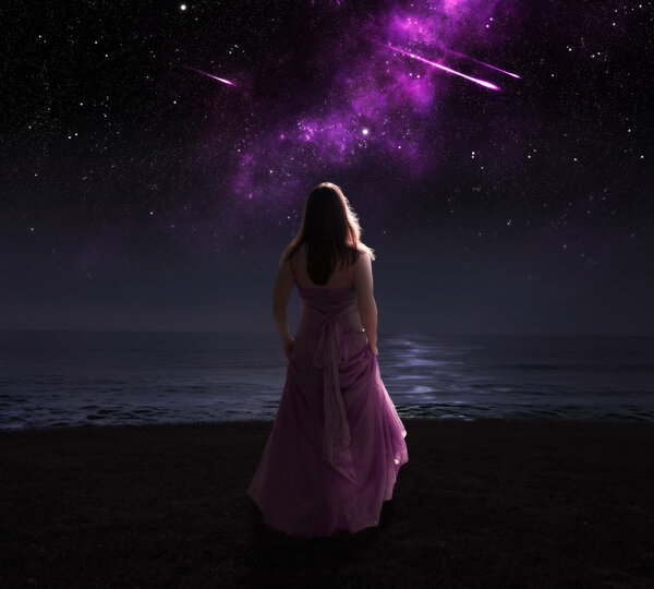 Woman standing in dress at night watching shooting stars.