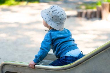 Kaydırağın arkasındaki çocuk, bir yaşındaki çocuk oyun parkında kaydırak kullanıyor.