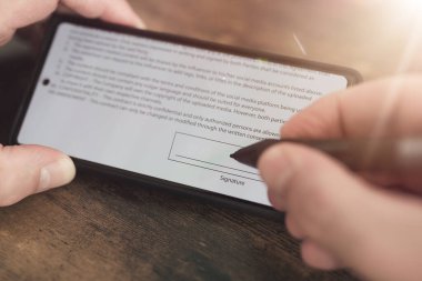 close-up view of electronic signature with stylus on smartphone screen against wooden table background