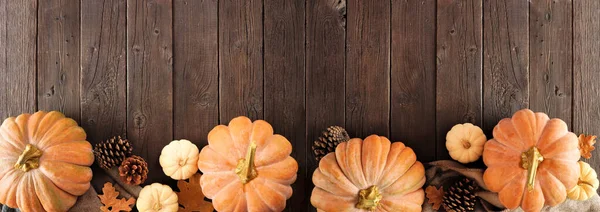 Cozy fall bottom border on a rustic dark wood banner background. Top view. Blanket, pumpkins and natural decor. Copy space.